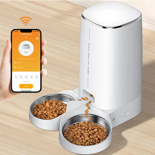 Smart pet feeder with two bowls of food and a smartphone displaying an app on a wooden surface.